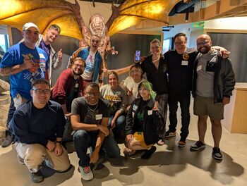 Fourteen members of the Commander Format Panel in front of Mitzy the Shivan Dragon.